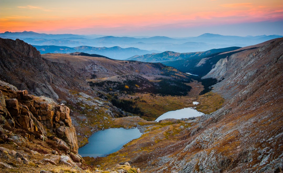 A vista of the Rocky Mountains, looking north from a rich near Summit Lake at Mount Evans. Smoke from wildfires raging in Boulder, CO shrouds the mountains as it drifts through the valleys, leaving only their peaks visible.